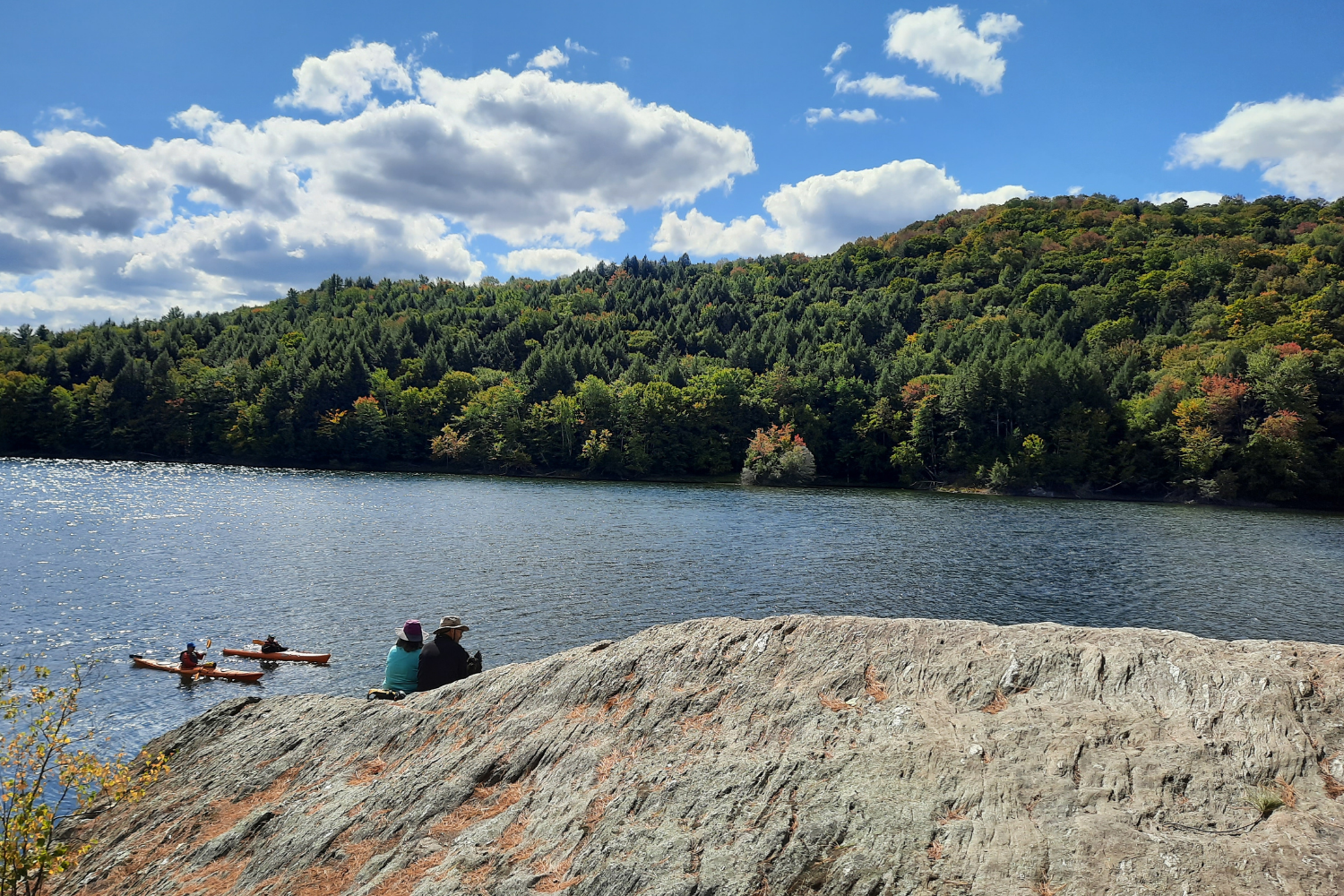 A couple sits on a rock overlooking kayakers in the Waterbury Reservoir